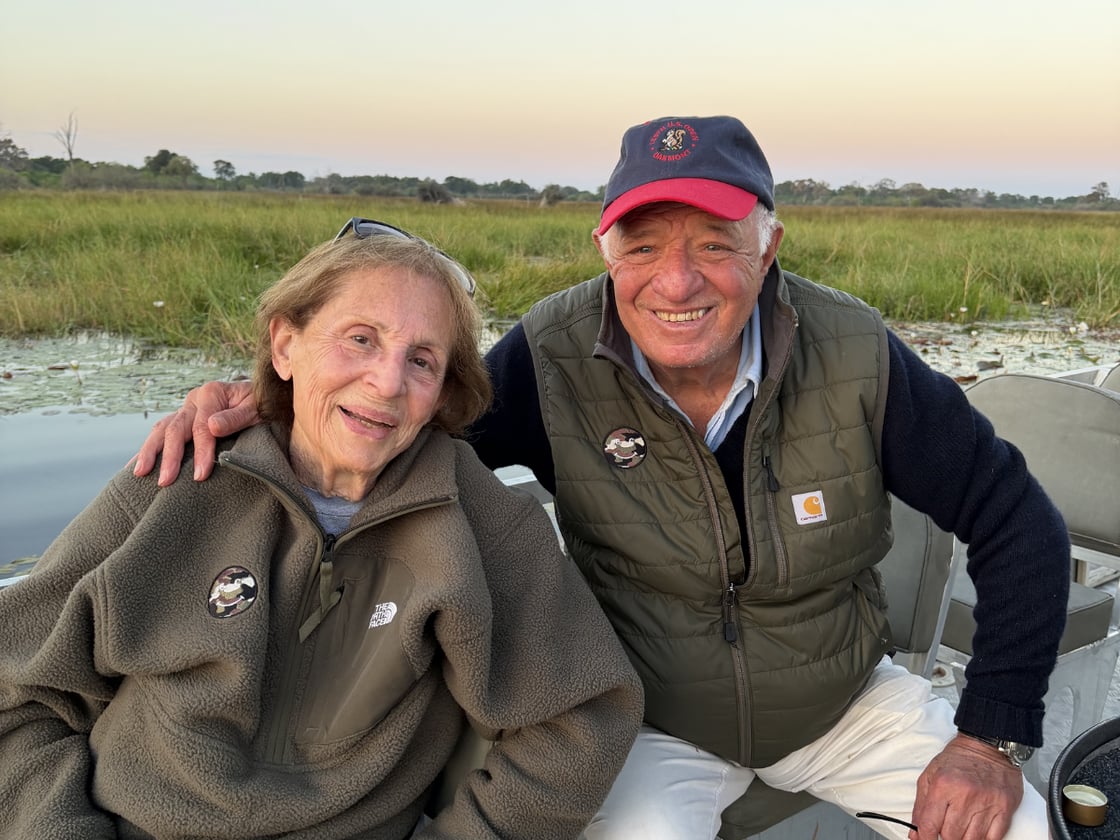 Two people smiling together on a boat at sunset, surrounded by the wetlands of the Okavango Delta in Botswana.